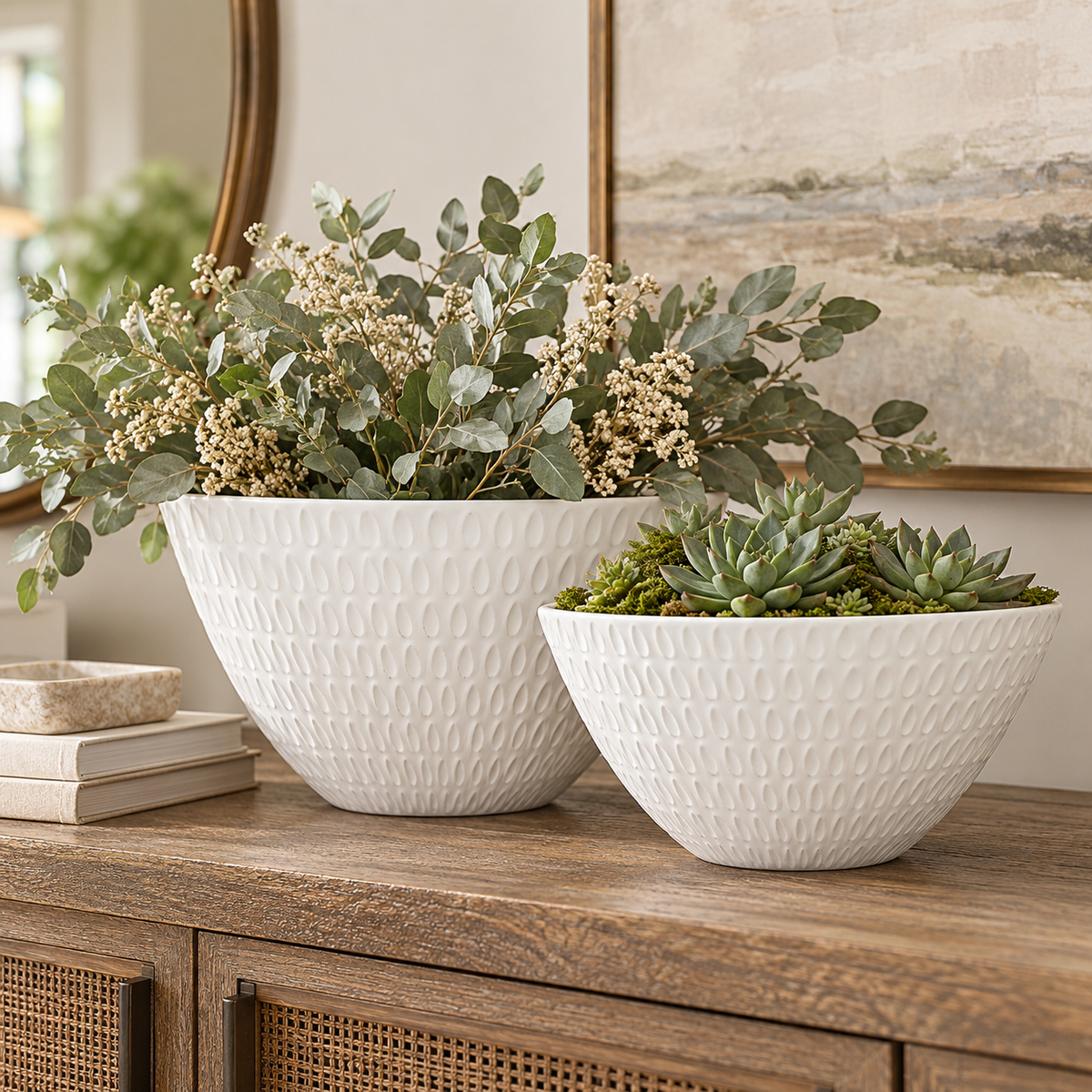Two white textured ceramic planters with leaf-like embossed patterns, one large and one small, filled with green foliage and succulents, displayed on a wooden console table in a styled interior setting.