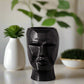 Black vase shaped like a face on a white background