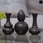 Three black ceramic vases on a reflective surface with a blurred background