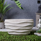 Textured stone planter on a grassy area with plants and a statue in the background
