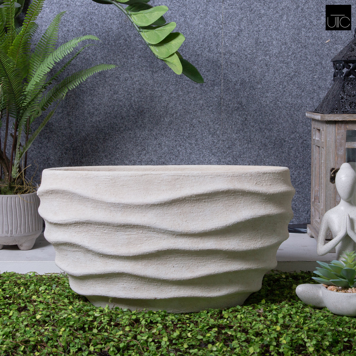 Textured stone planter on a grassy area with plants and a statue in the background