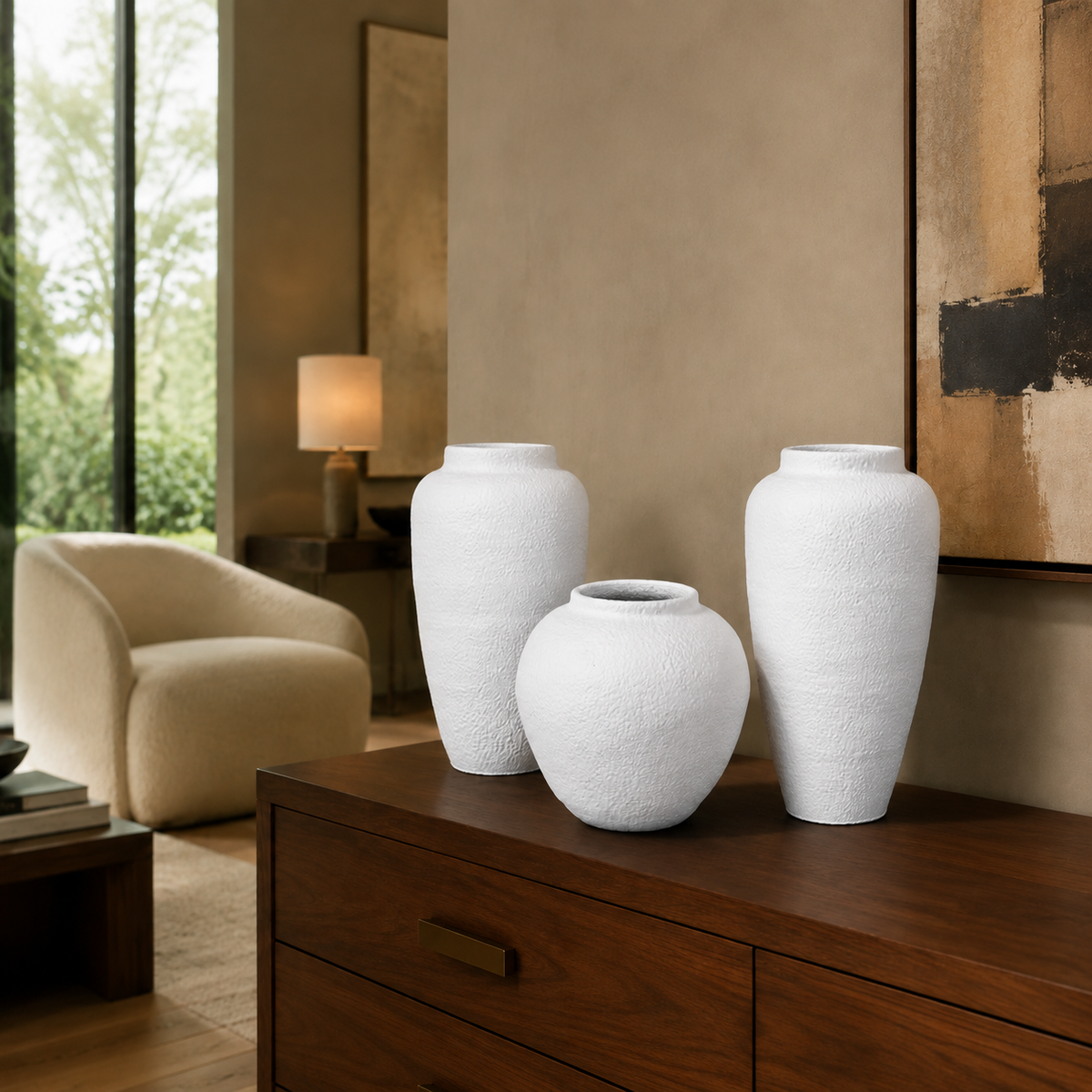 Three white textured ceramic vases of different heights displayed on a dark wood console table in a modern, neutral-toned living room.