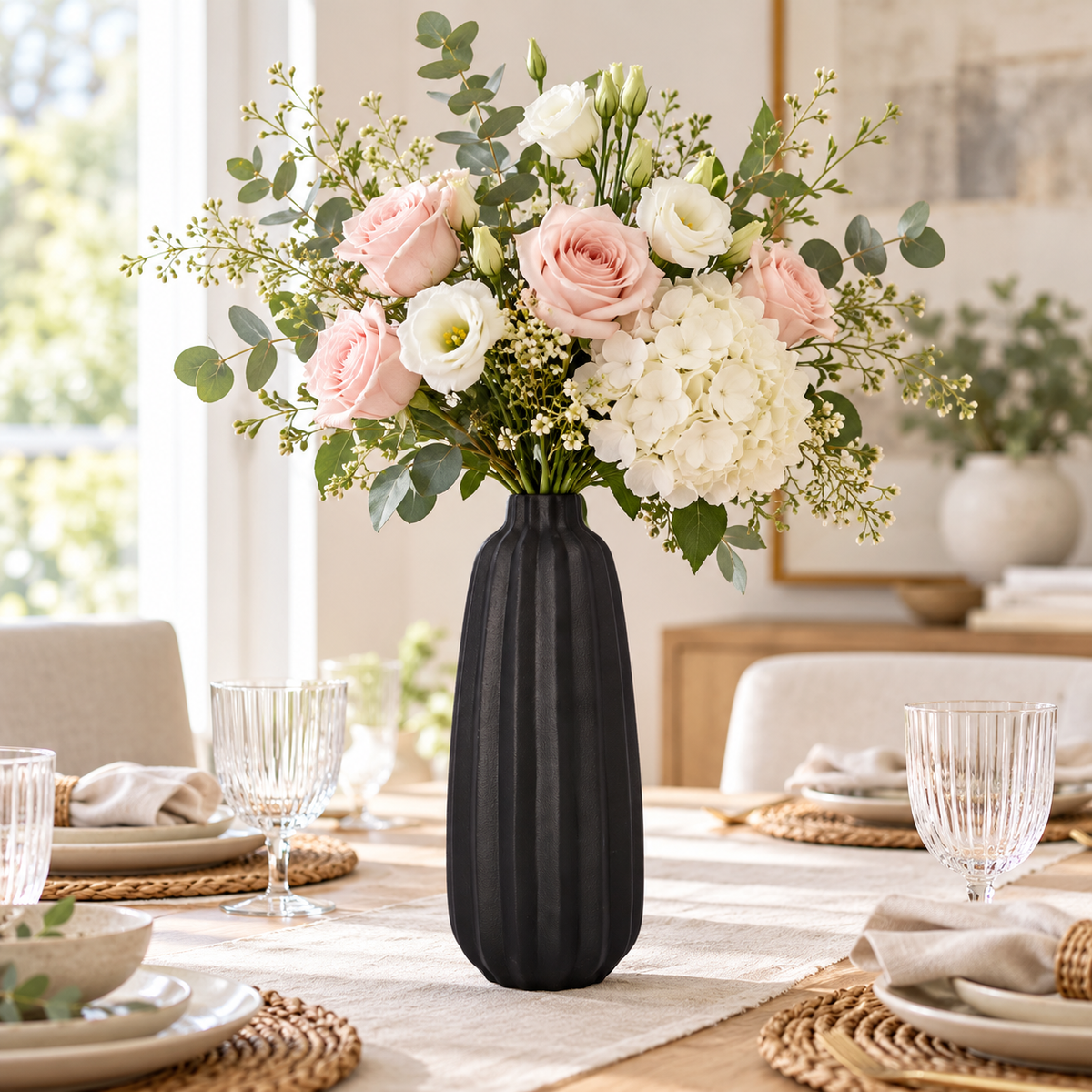 A black ribbed ceramic vase filled with a floral arrangement of pink and white roses, white lisianthus, and green eucalyptus, displayed on a dining table in a bright, modern dining room.