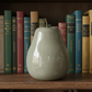White ceramic vase on a wooden shelf with books in the background