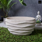 Textured stone planter on grass with plants and a statue in the background