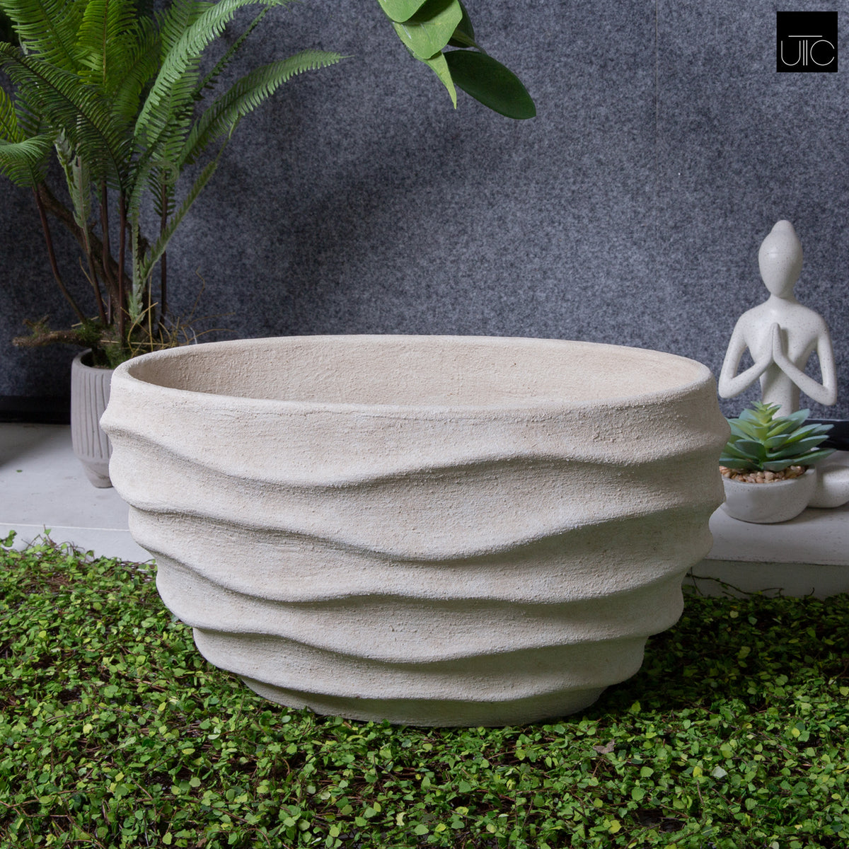 Textured stone planter on grass with plants and a statue in the background