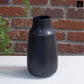 Black vase against a brick wall with greenery
