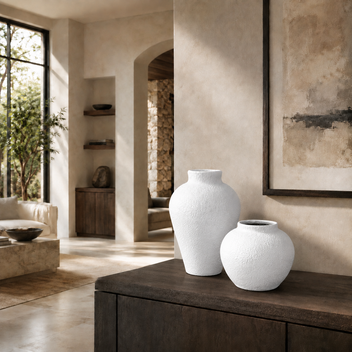 Two textured white ceramic vases, one tall and one short, displayed on a dark wooden console table in a warm, modern rustic interior.
