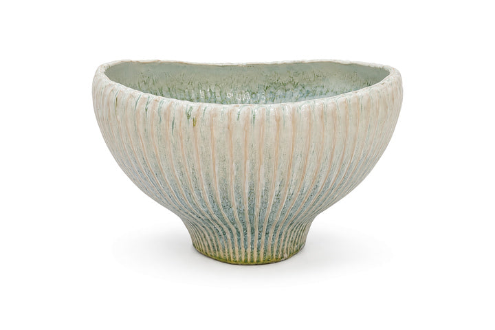 A handmade ceramic bowl with a ribbed, sunburst texture, featuring a glaze that transitions from a light cream-beige at the top to a textured light blue-green and earthy brown at the base, set against a plain white background.
