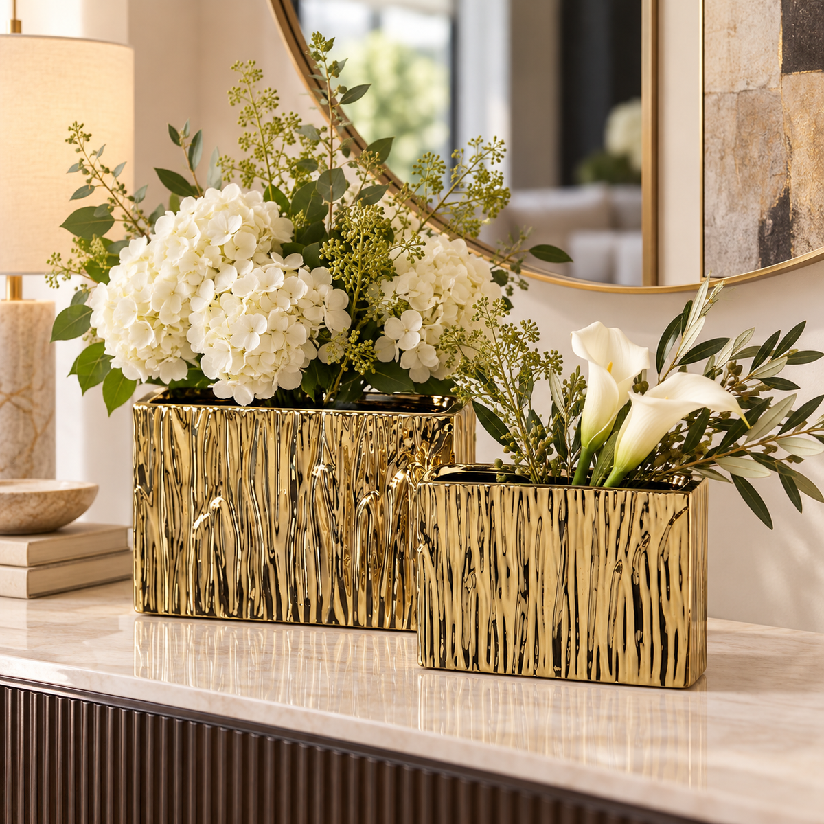 Two rectangular gold ceramic vases with a textured, tree-bark-like vertical pattern, filled with white flowers and green foliage, displayed on a marble console table in a modern interior setting.