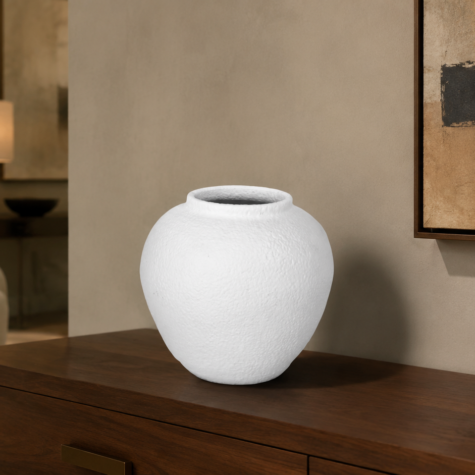 A white textured ceramic vase displayed on a dark wood console table in a modern, neutral-toned living room setting.