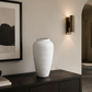 A tall, textured white ceramic vase displayed on a dark wooden console table in a modern, minimalist interior hallway.