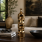 A tall, textured metallic gold decorative vase with a honeycomb-like circular pattern, displayed on a dark wooden coffee table in a modern living room setting.
