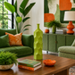 A styled living room scene featuring a tall, textured lime green ceramic vase as the central product, placed on a wooden coffee table alongside books, a small orange bowl, and potted plants. The background includes a green velvet sofa, a green cabinet, and a matching green armchair.