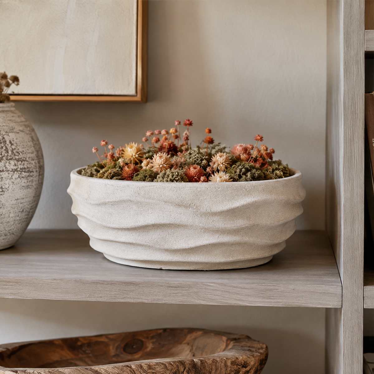 A textured off-white ceramic planter with wavy ridges, filled with small orange and green succulents, displayed on a light gray wooden shelf.
