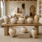 A set of rustic, earth-toned ceramic vases displayed on a wooden table and pedestal in a beautifully styled, neutral-toned living room.
